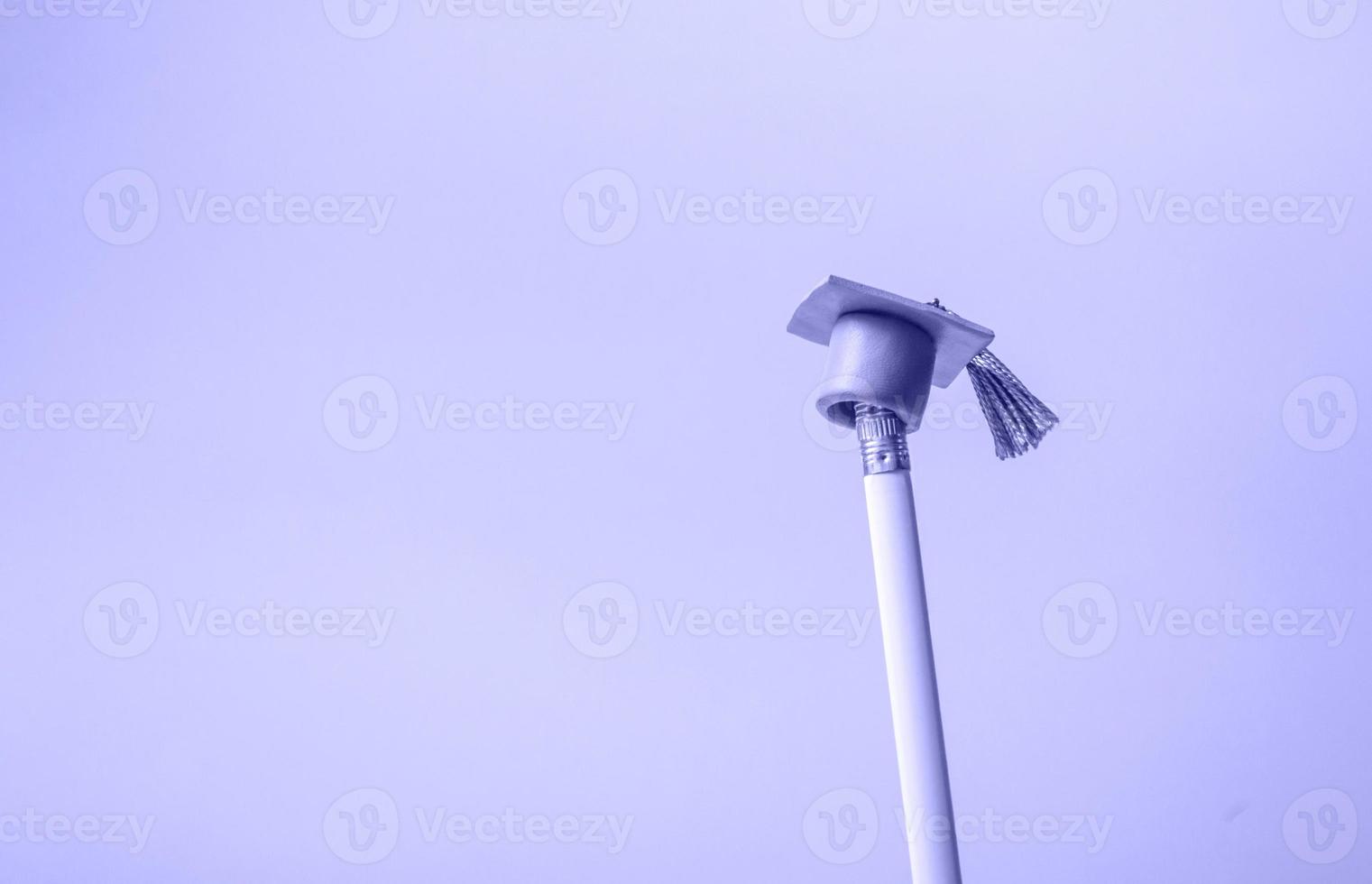 White pencil with graduation hat on a very peri background closeup with copy space. Education concept photo