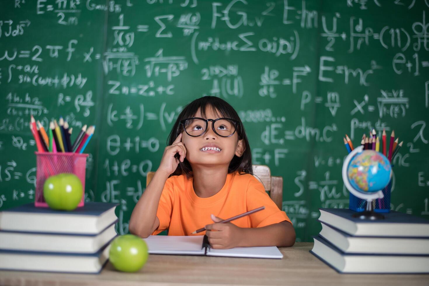 Thoughtful little girl with book near a school board photo