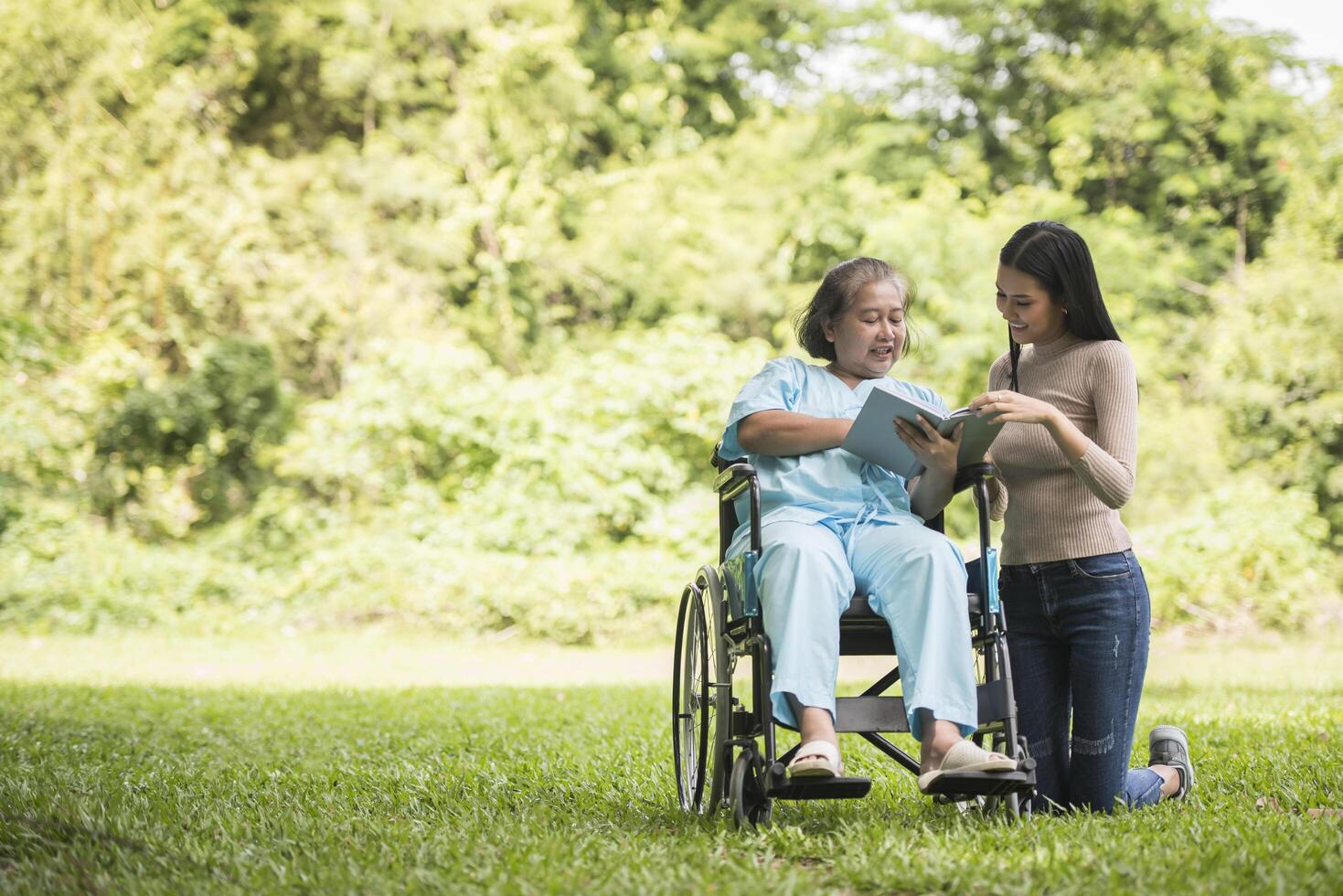 Happy Woman in a wheelchair reading a book with her daughter at the park photo