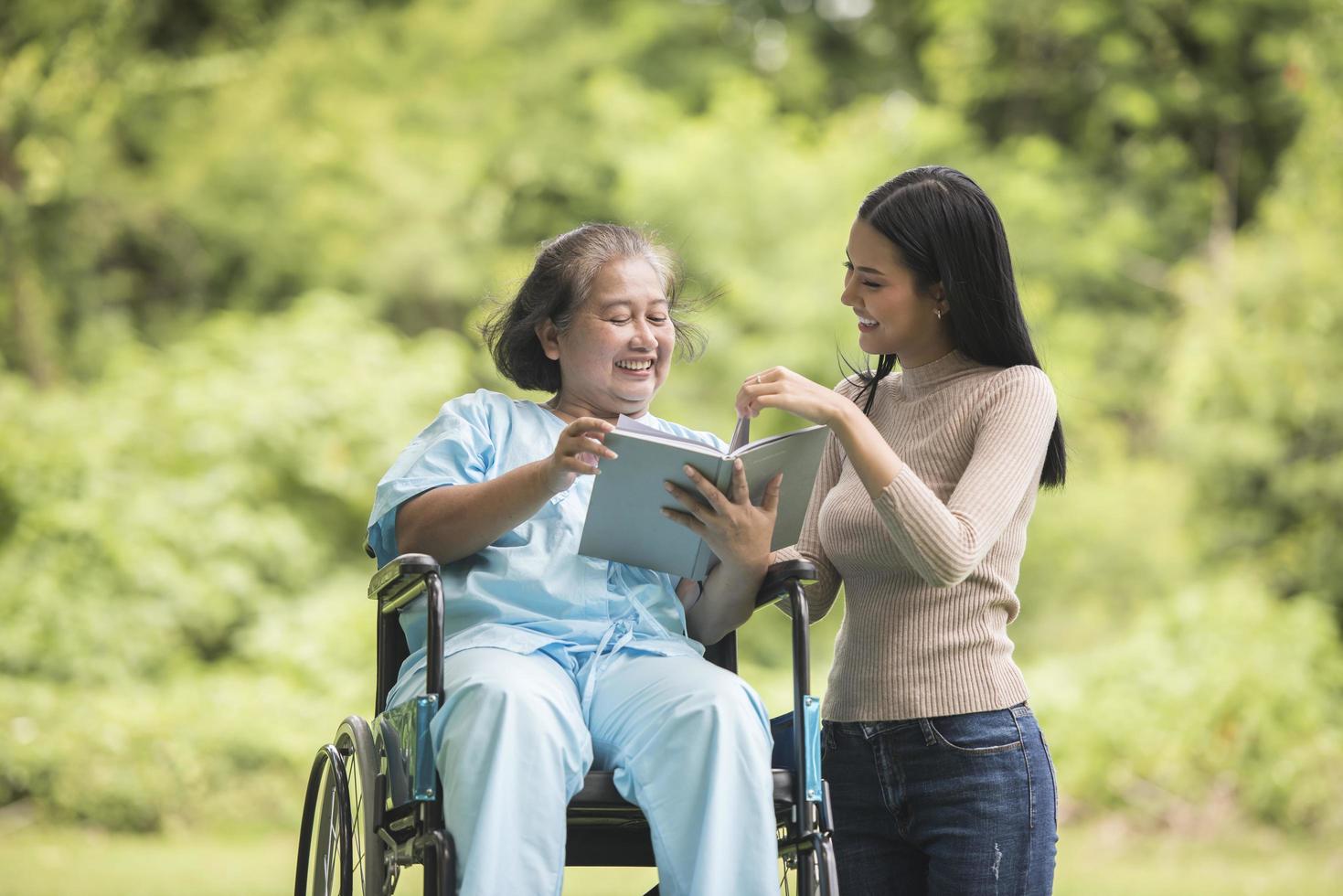 Happy Woman in a wheelchair reading a book with her daughter at the park photo