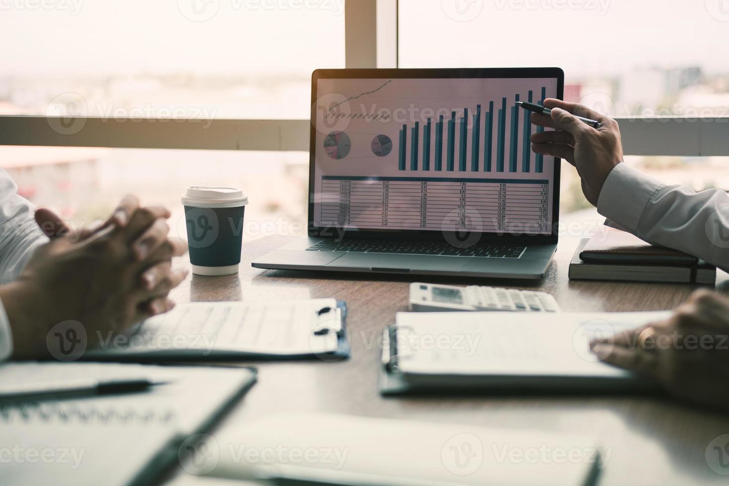 Male manager is explaining about the company cost graph on the laptop computer for employees to listen to and share the analysis together. photo