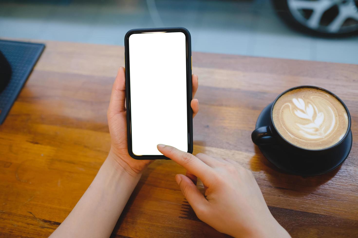 imagen de una maqueta de las manos de una mujer sosteniendo un teléfono móvil blanco con una pantalla en blanco en el muslo y una taza de café en la cafetería. foto
