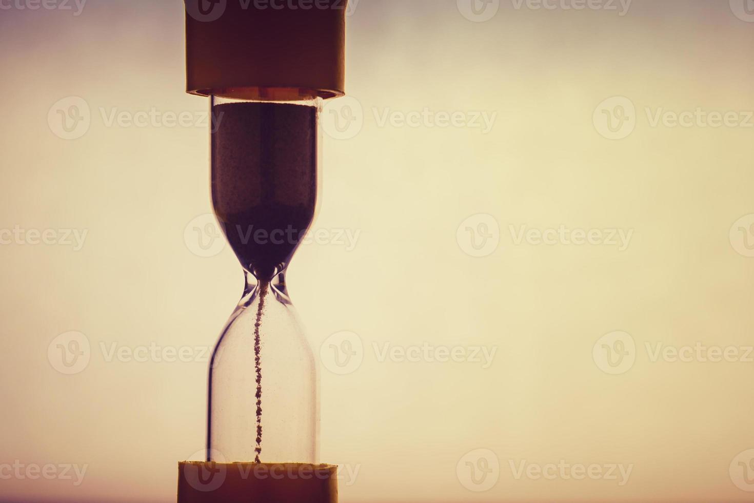 Sand running through the bulbs of an hourglass on light background with copy space photo