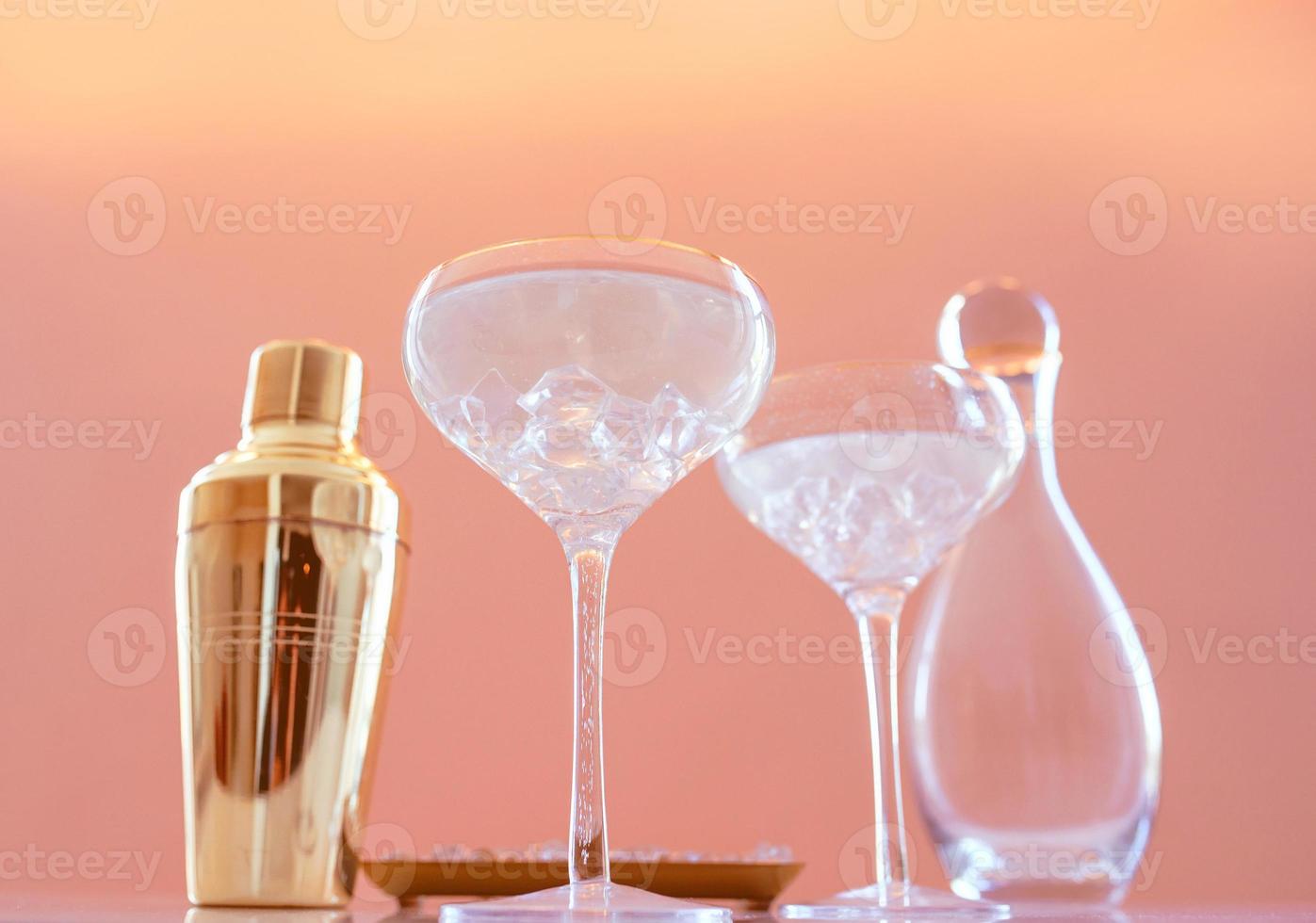 agitador dorado, decantador de vidrio, vasos elegantes con cóctel y hielo sobre fondo beige. alcohol, fiesta, hotel, bar concepto foto