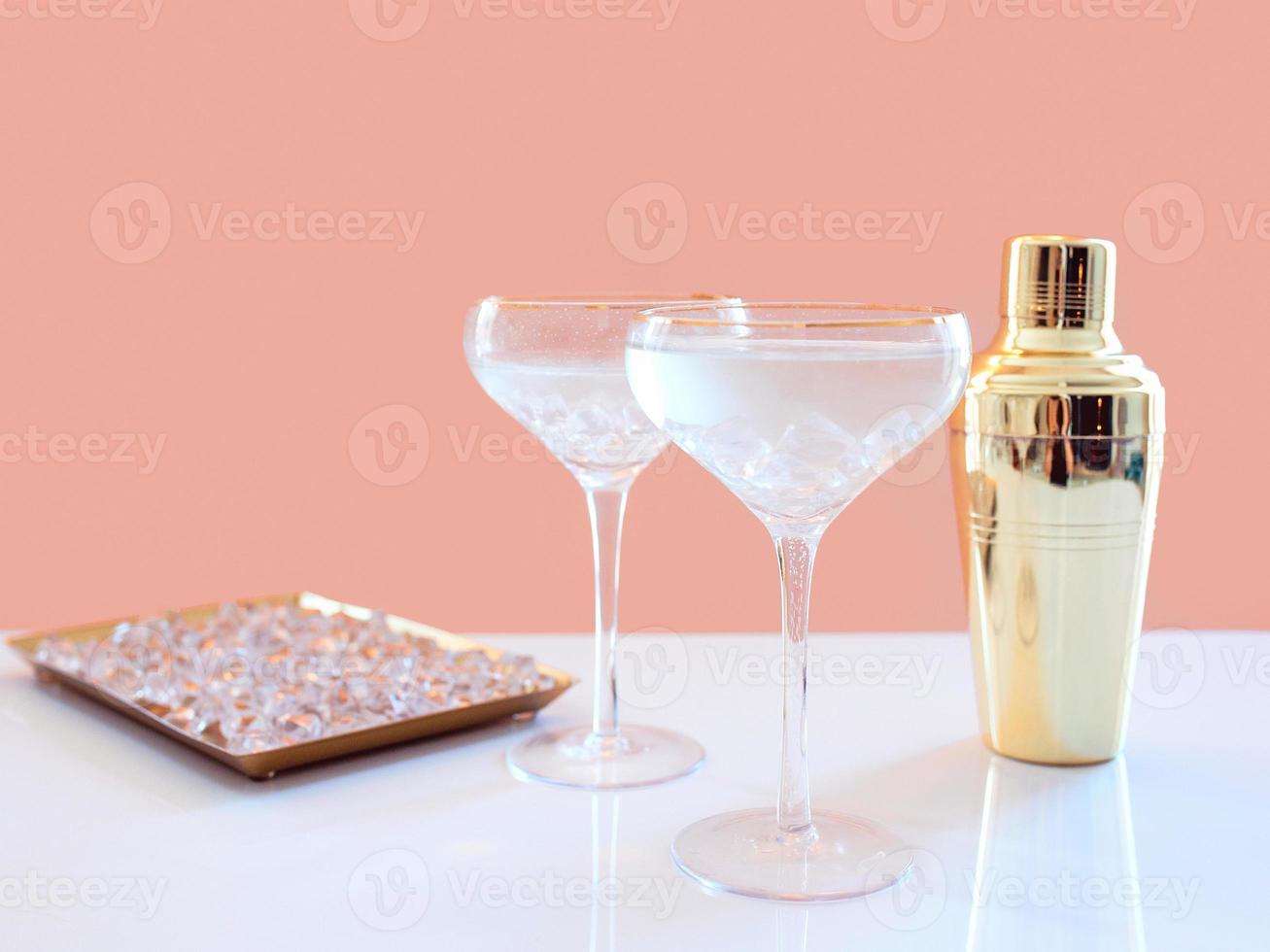 golden shaker, glass decanter, elegant glasses with cocktail and ice on beige background. Alcohol, party, hotel, bar concept photo