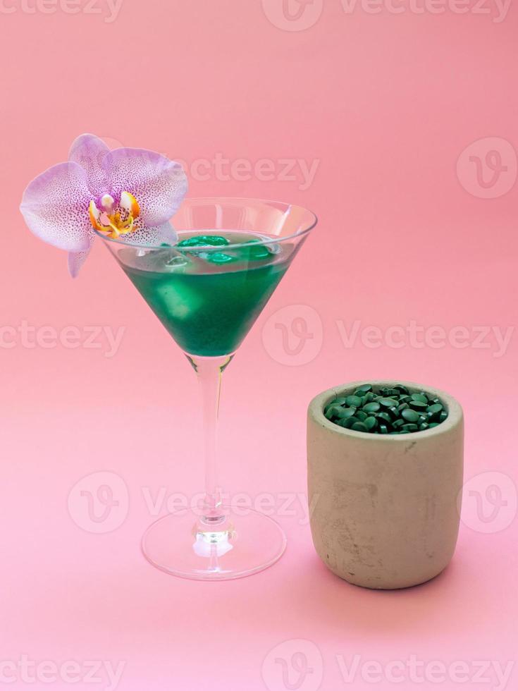 Liquid spirulina green drink in cocktail glass and spirulina pills on pink background. Super food, healthy lifestyle, healthy supplements concept photo