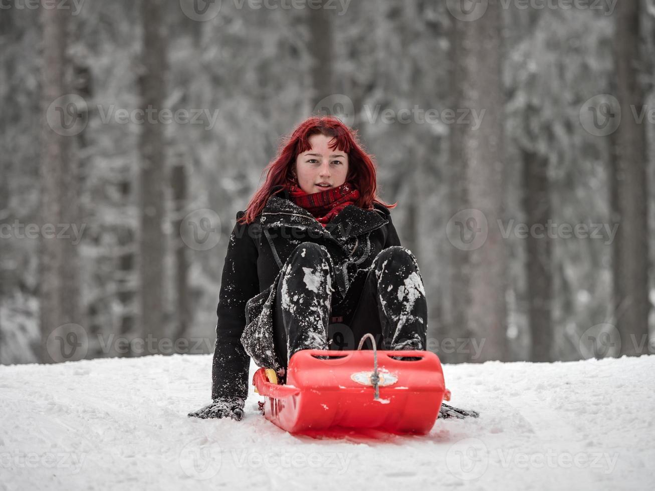 A girl with red hair sleds on the winter snow in the forest. photo