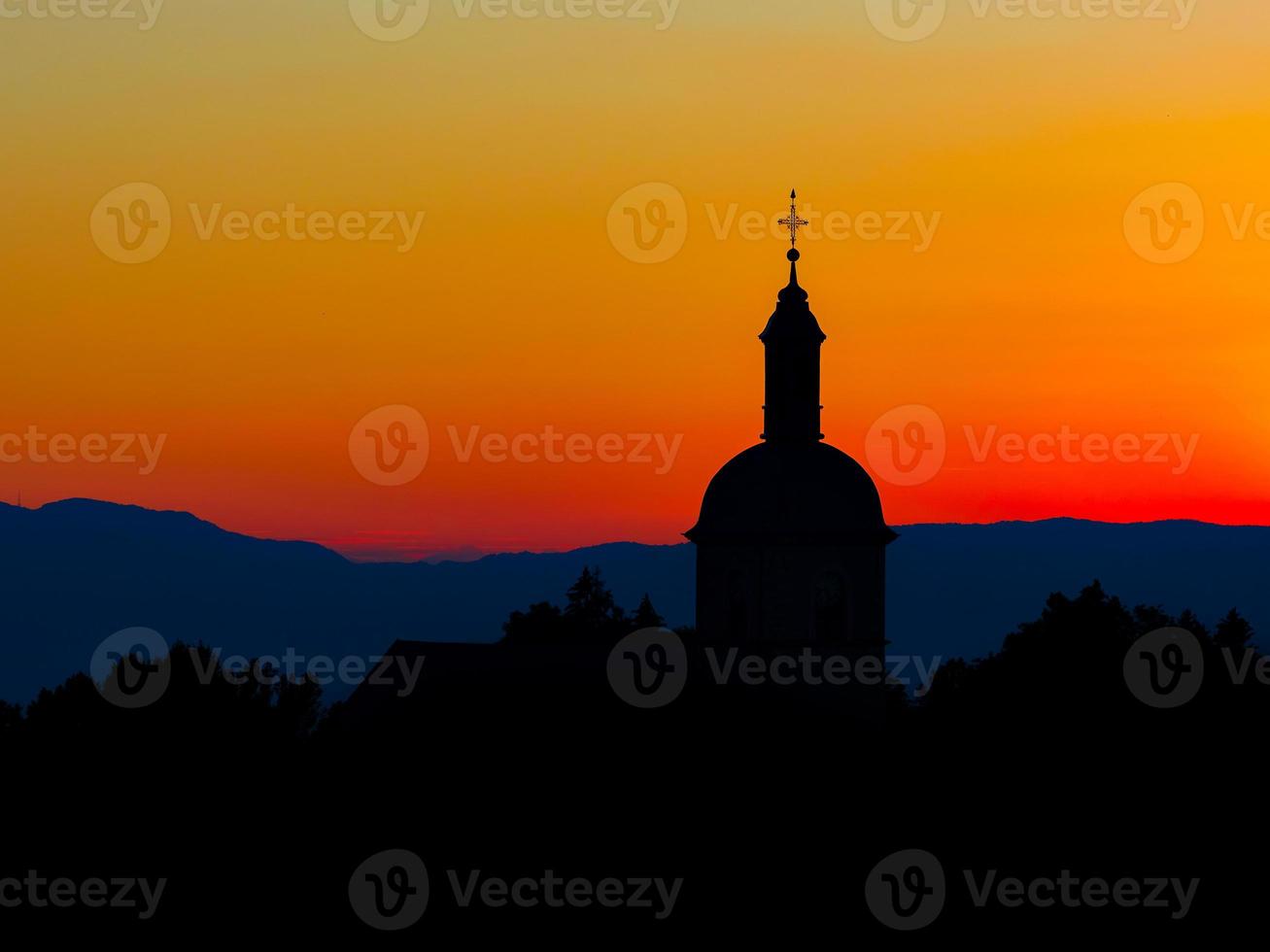 The stunning beauty and colors of the sunset overlooking the silhouettes of the Alps and the silhouette of a beautiful church photo