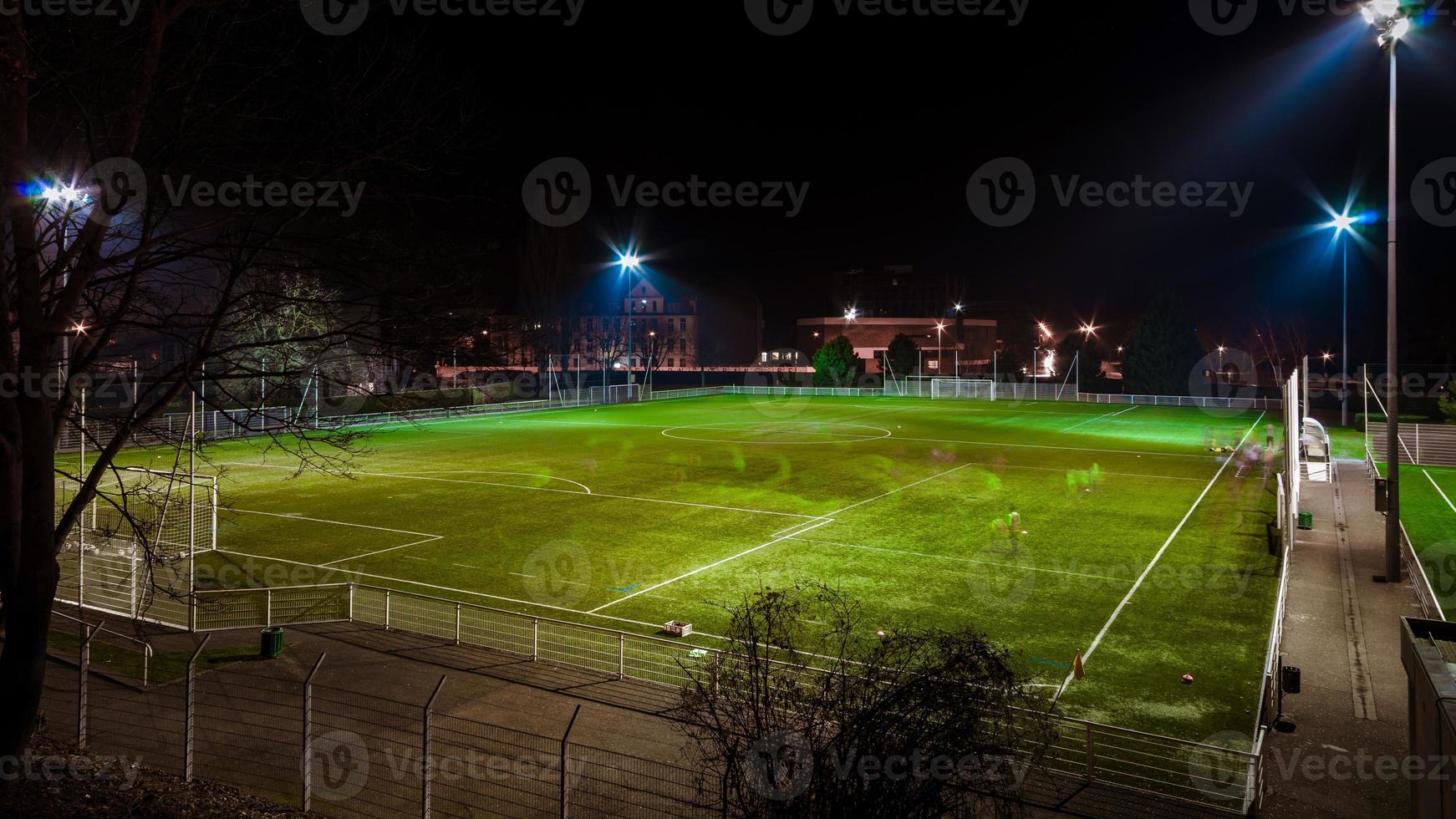 campo de fútbol verde resaltado en la noche con tres personas corriendo foto