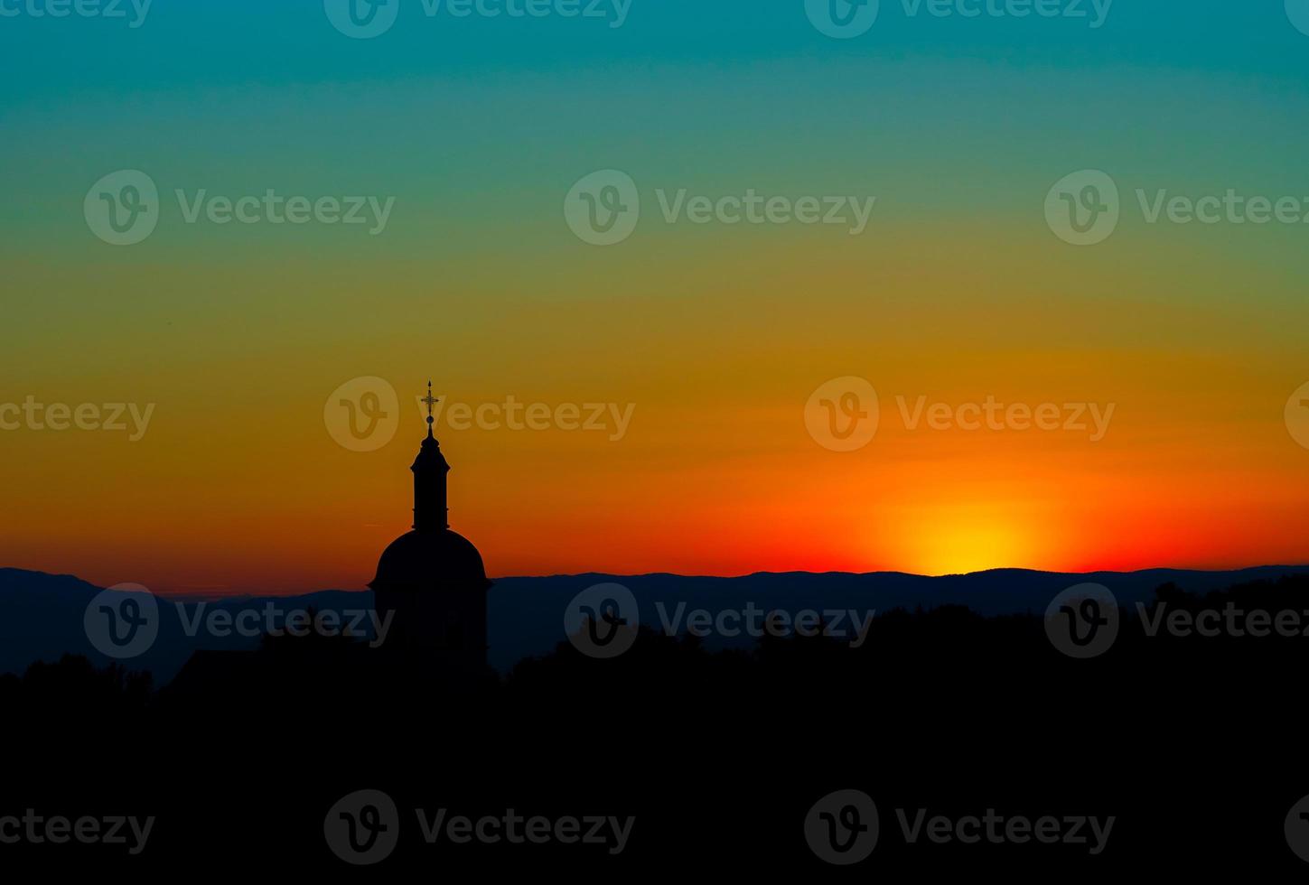 The stunning beauty and colors of the sunset overlooking the silhouettes of the Alps and the silhouette of a beautiful church photo