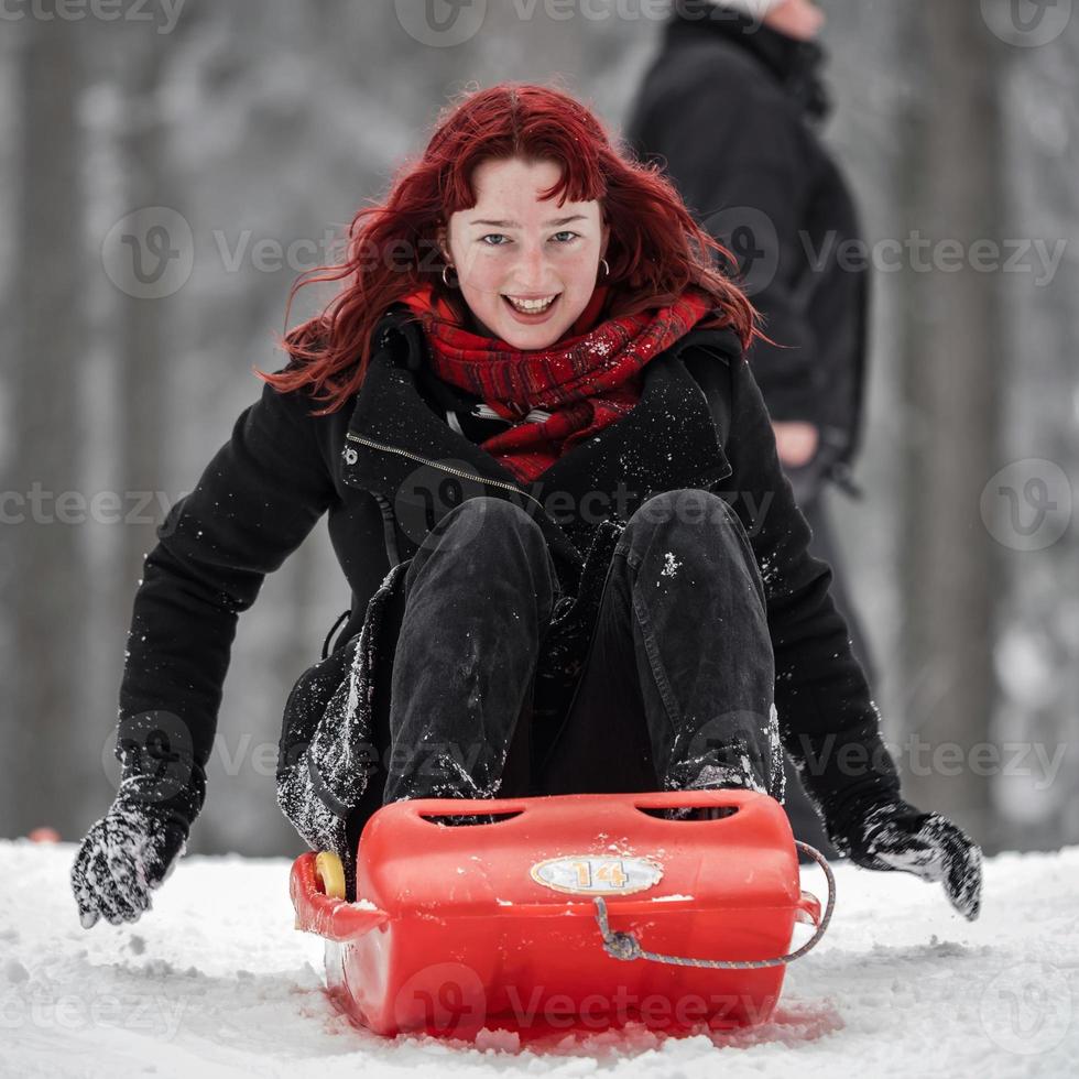 A girl with red hair sleds on the winter snow in the forest. photo