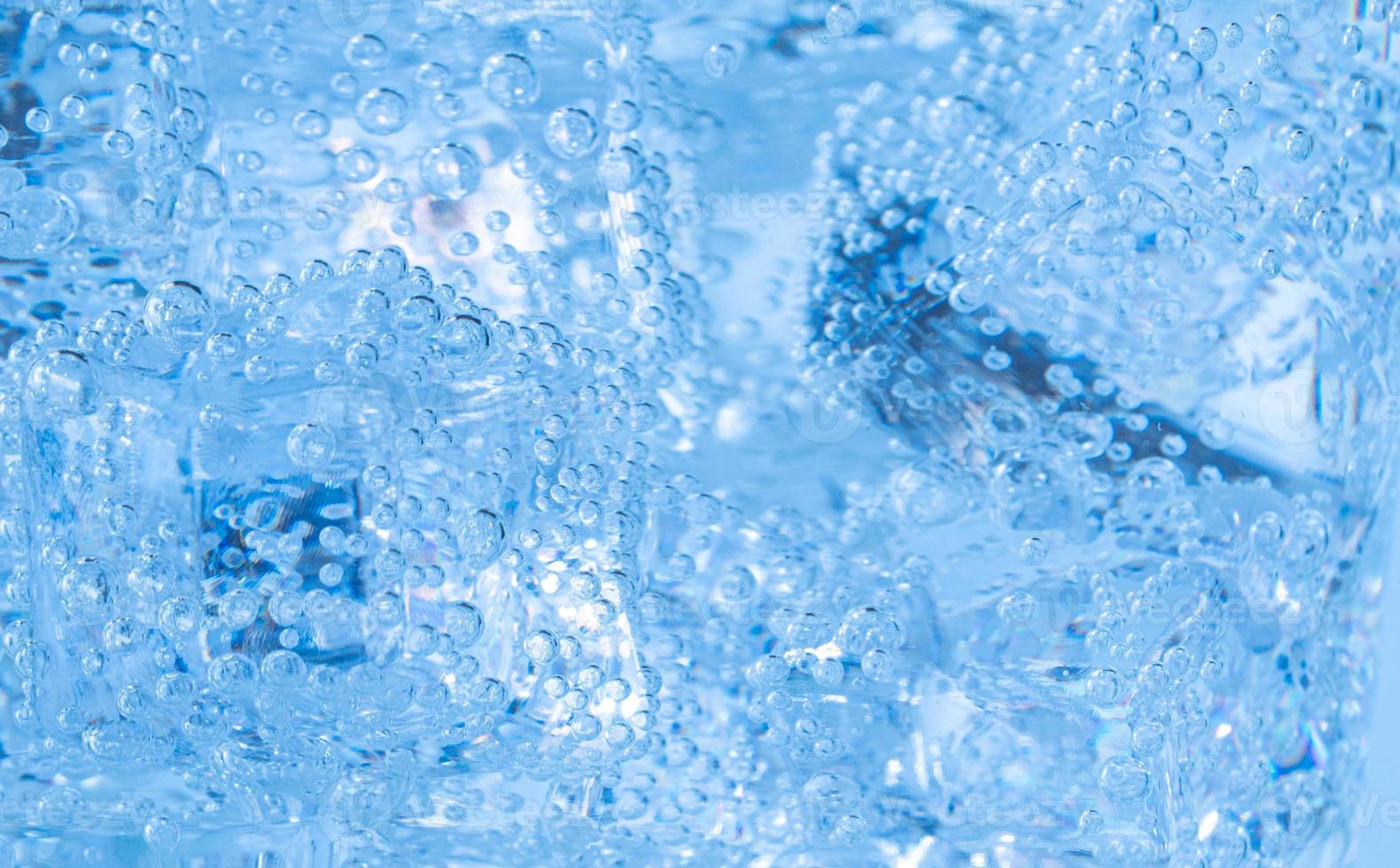 los cubitos de hielo con burbujas de aire se arremolinan en el vaso. agua de soda y enfriar en un vaso transparente. foto