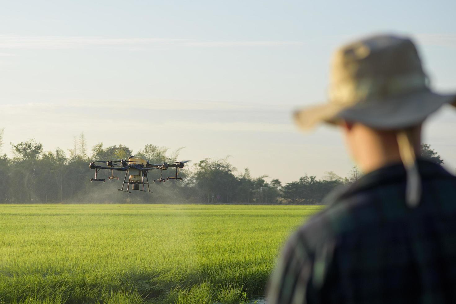 Young smart farmer controlling drone spraying fertilizer and pesticide over farmland,High technology innovations and smart farming photo