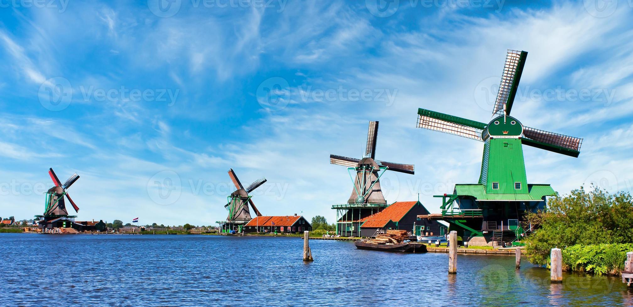 Molino de viento holandés en un campo verde cerca de Amsterdam, Países Bajos, con cielo azul y agua de río. foto