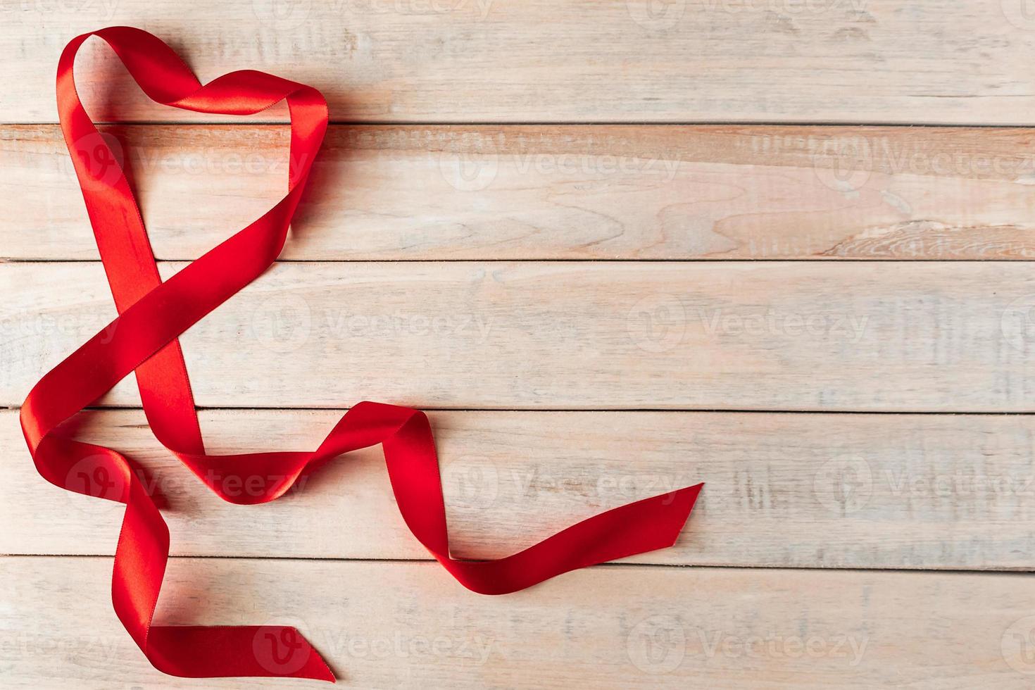 Red silk ribbon in shape of a heart on a wooden background. photo