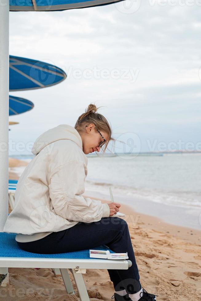 young woman artist painting or doing travel sketches using watercolor by the seaside photo