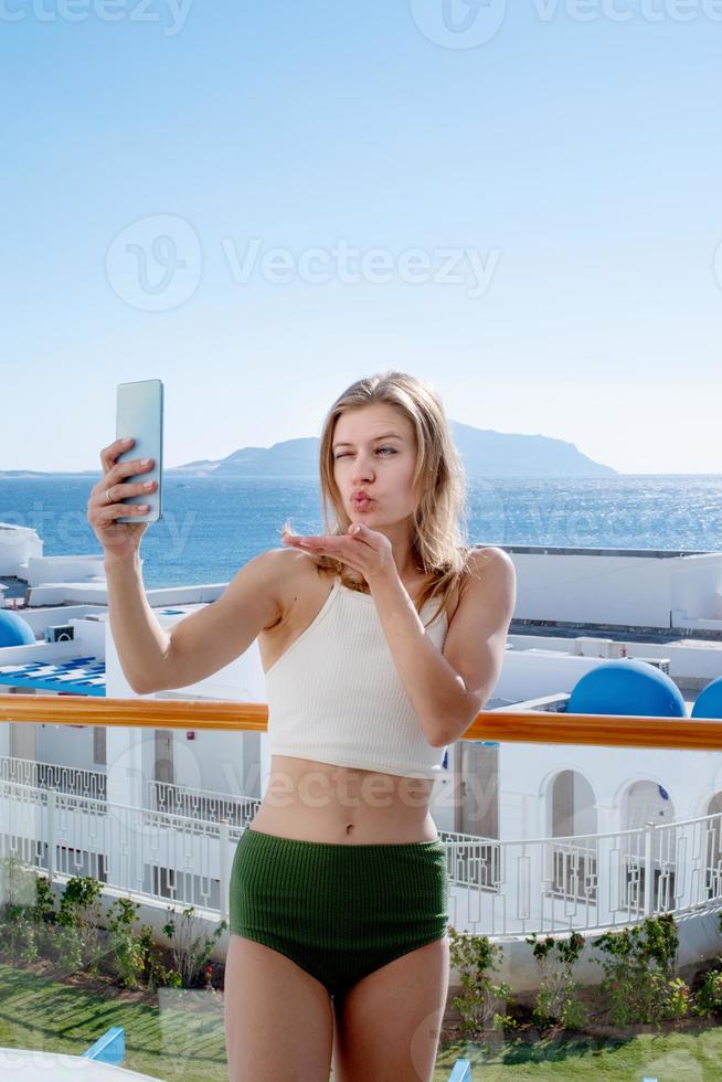 Happy woman in swimsuit taking selfie standing on the balcony of the hotel room photo