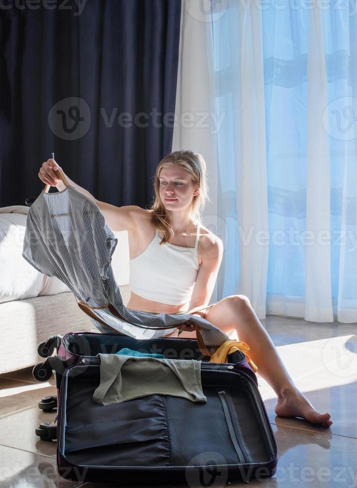 emocionada joven mujer caucásica empacando bolsas para vacaciones foto