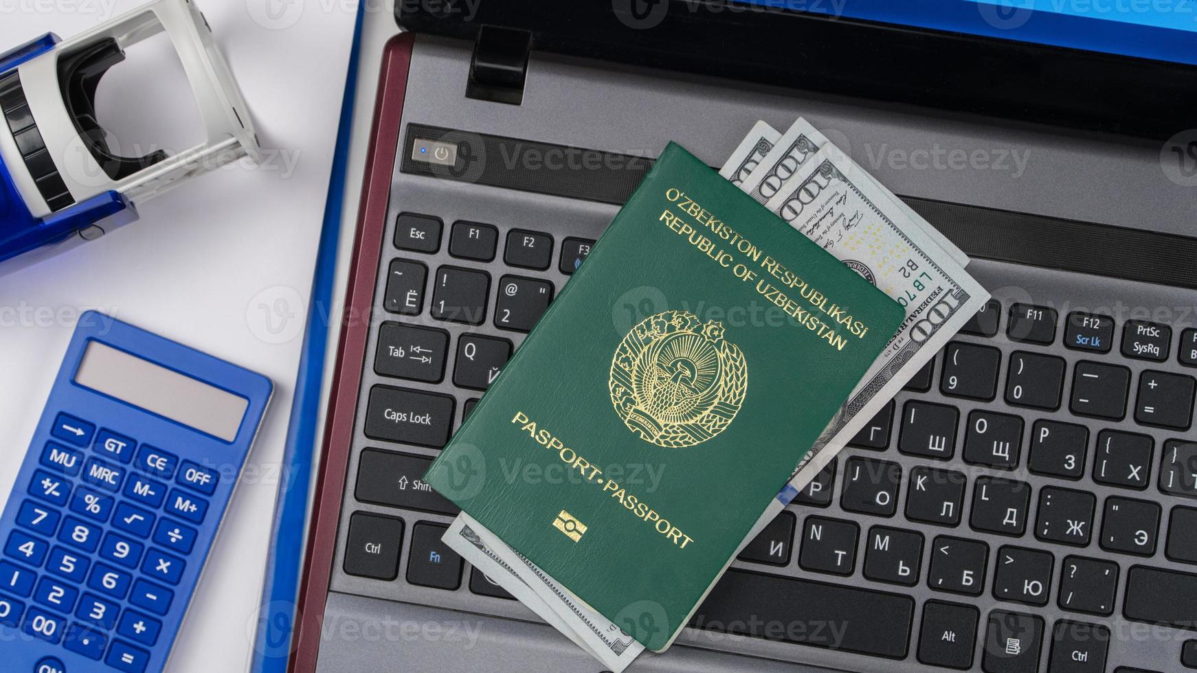 pasaporte de uzbekistán con dólares estadounidenses en el teclado de la computadora portátil. Registro en línea. concepto - soborno y corrupción. vista superior foto