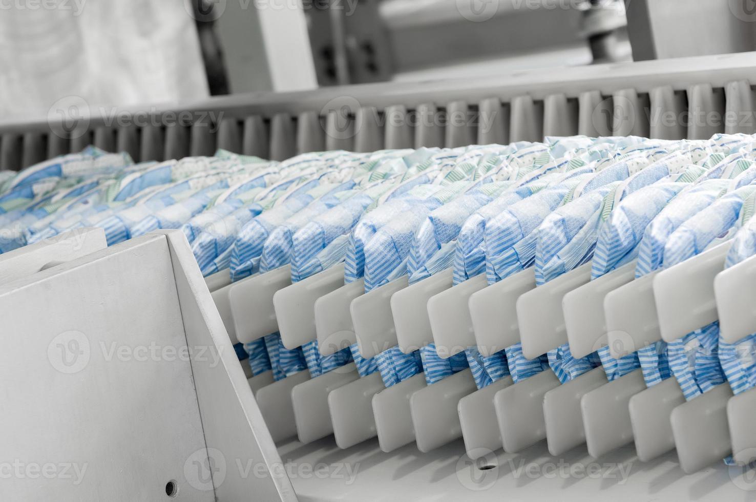 diapers on a conveyor belt closeup. factory and equipment for the production of pampers photo