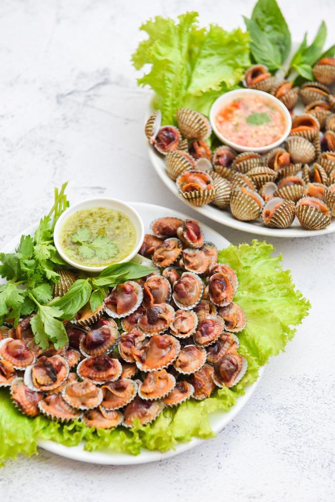 berberechos pelados con salsa de marisco y lechuga de ensalada de verduras sobre fondo de plato blanco, marisco fresco crudo sangre berberecho marisco gourmet en el restaurante, comida de conchas marinas foto