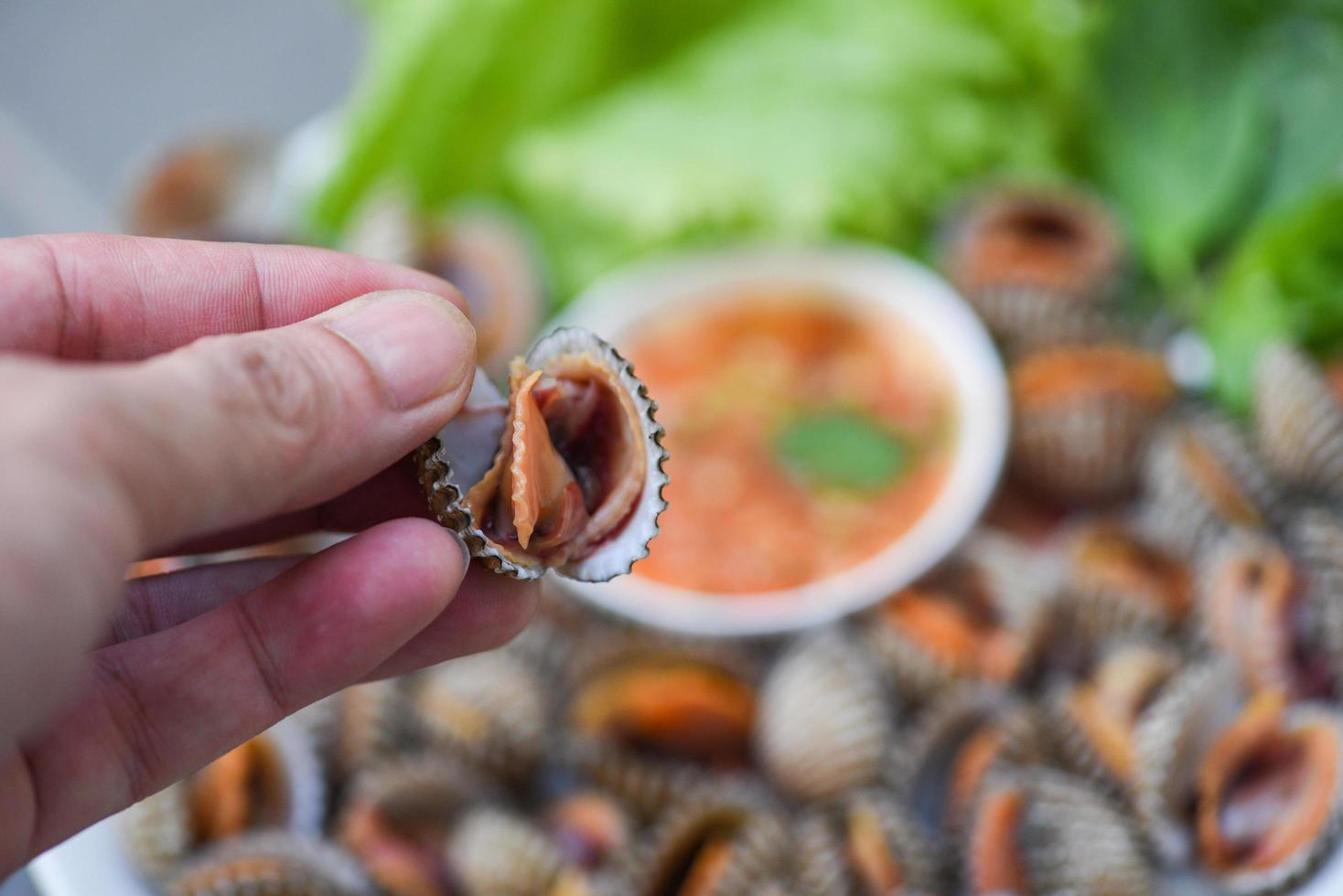 berberechos pelados a mano con salsa de marisco y lechuga de ensalada de verduras en el fondo del plato, marisco fresco crudo sangre berberecho marisco gourmet en el restaurante, comida de conchas marinas foto