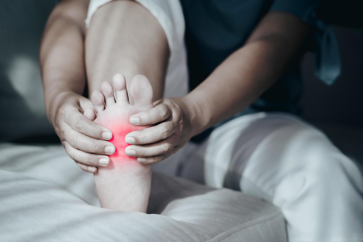 Woman sitting on the sofa and holding her foot suffering from foot pain with red highlight, massaging her painful foot, Healthcare and medical concept. photo