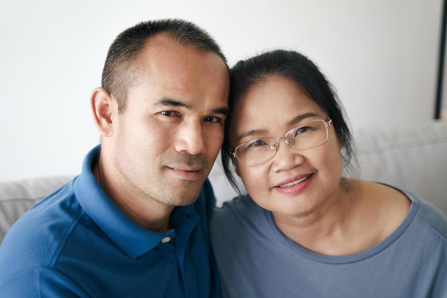 Portrait of Asian mature couple sitting in the living room. wife and husband hugging, holding hand with happiness and cheerful. Love, safety, and insurance family concept photo