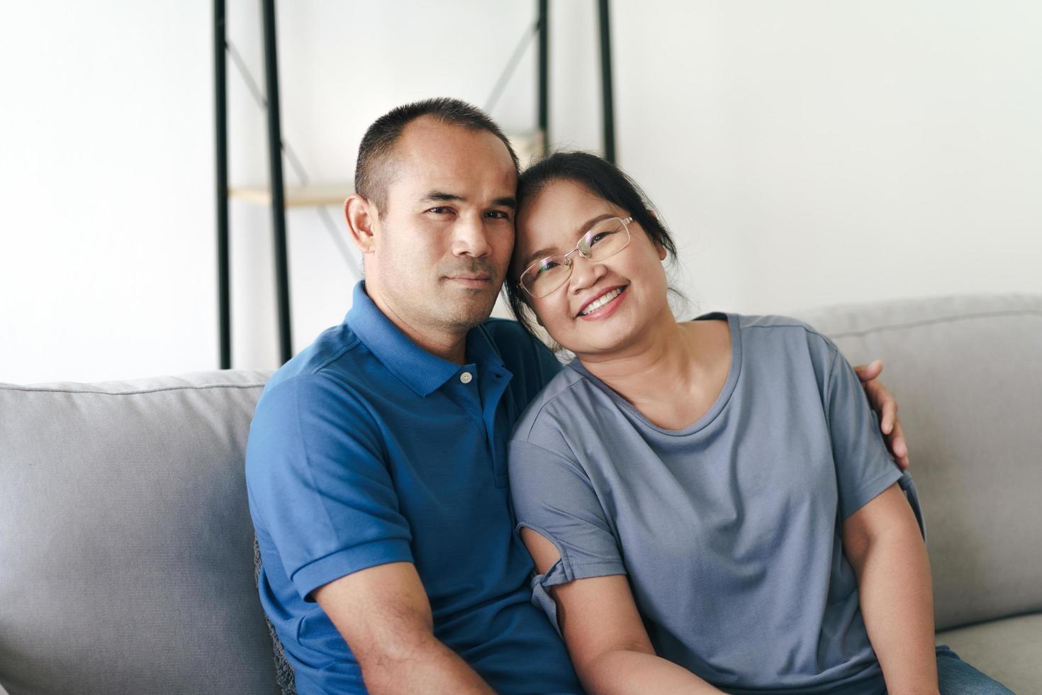 Portrait of Asian mature couple sitting in the living room. wife and husband hugging, holding hand with happiness and cheerful. Love, safety, and insurance family concept photo
