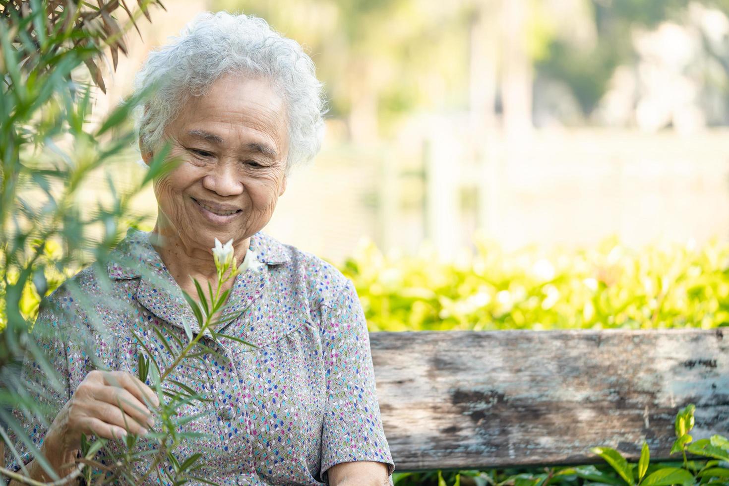 anciana asiática o anciana sosteniendo una flor rosa roja, sonriendo y feliz en el jardín soleado. foto