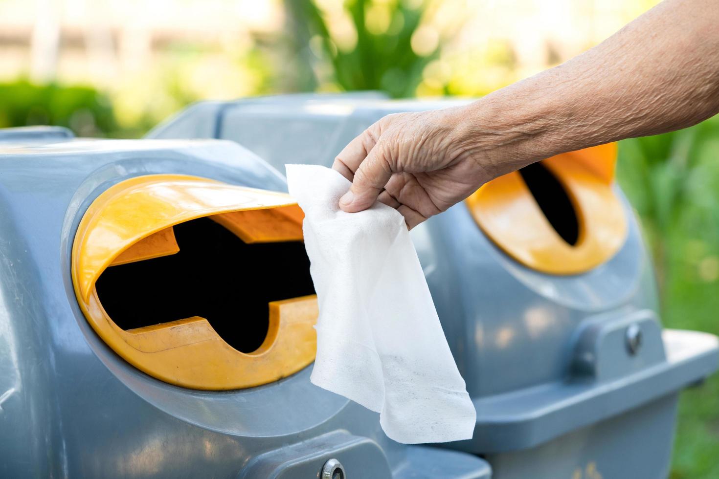 Elderly woman throwing wet wipe into recycling bin at park. photo