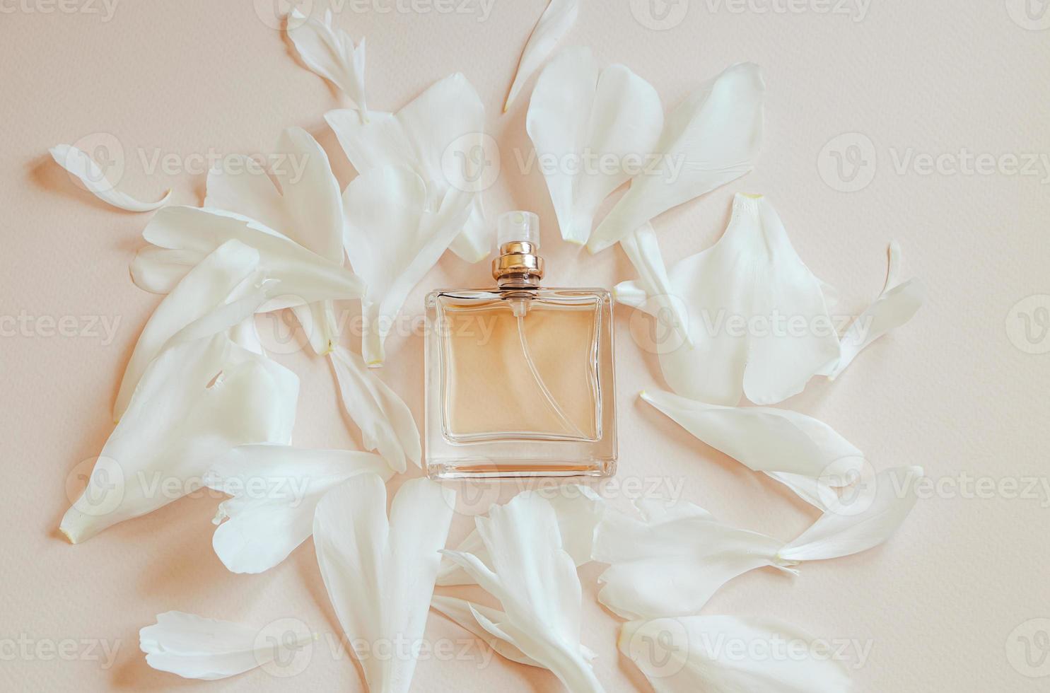 Perfume bottle and flower petals on pastel beige background. Natural cosmetics with aromatic oil. photo