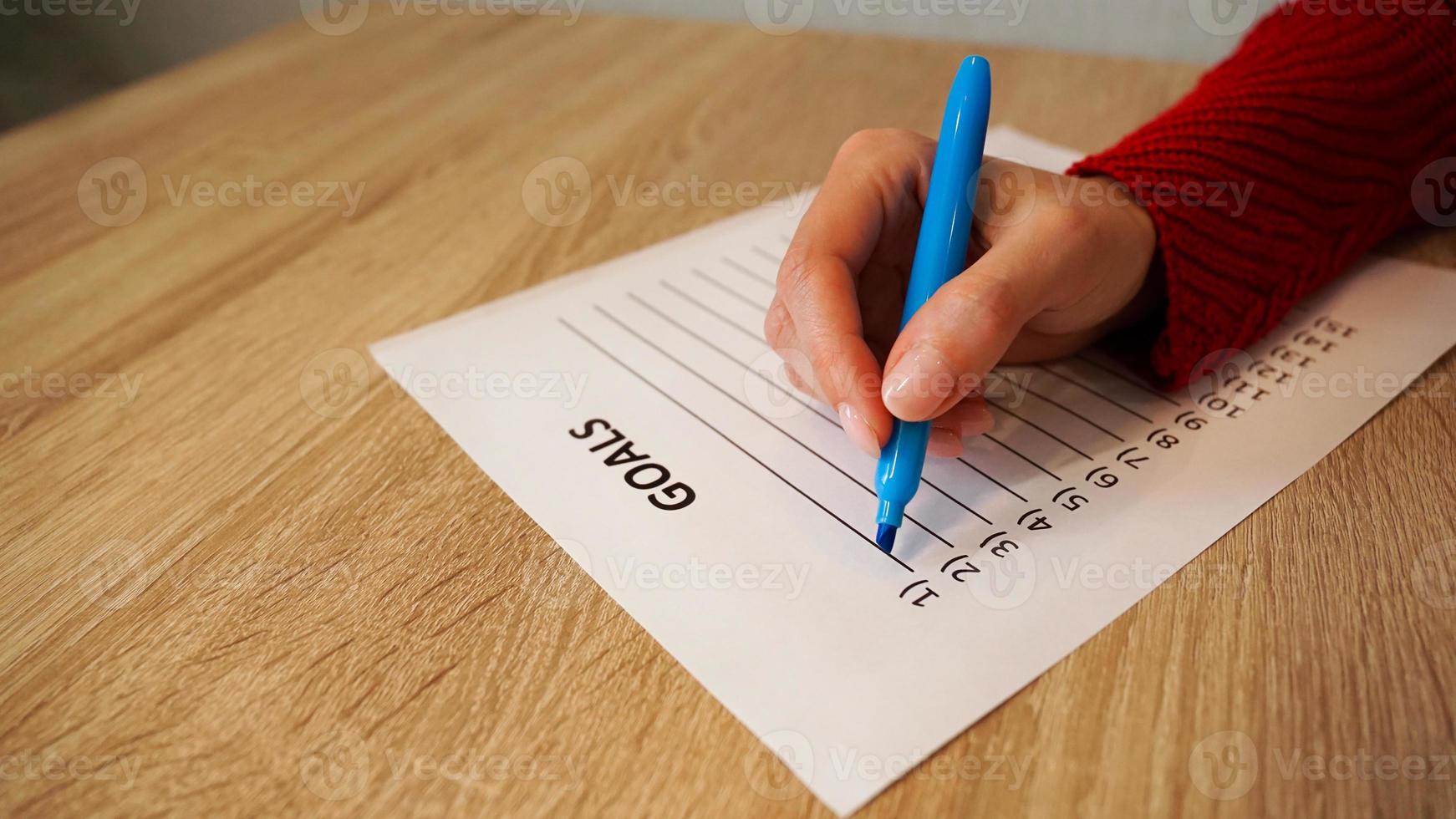 Woman writing down her goals list by blue marker photo