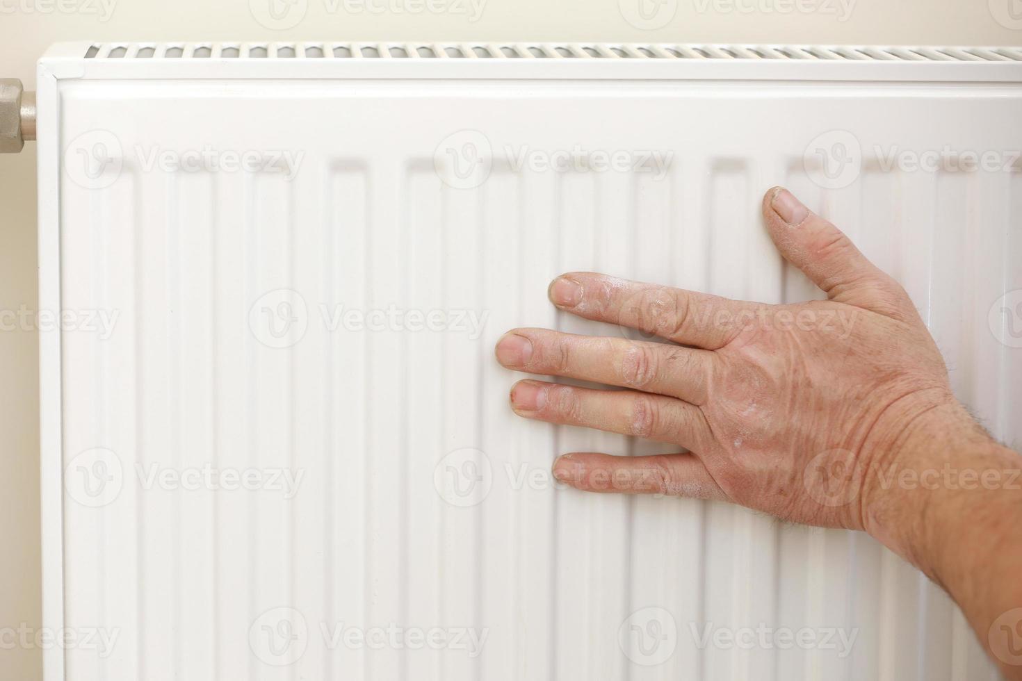 hombre en overoles de trabajo usando una llave mientras instala un radiador de calefacción en la habitación. fontanero instalando sistema de calefacción en apartamento. concepto de instalación de radiadores, trabajos de plomería y renovación de viviendas foto