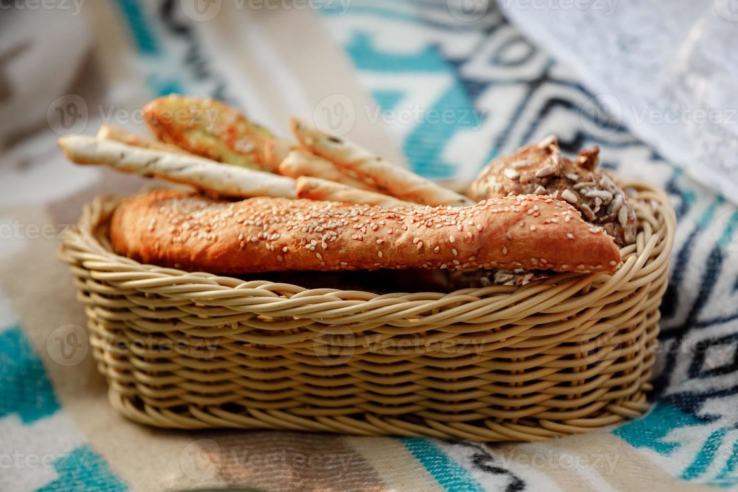 cesta de mimbre con pan. pan, bollos y grissini dentro de la cesta. productos de panadería frescos en un picnic. enfoque selectivo foto