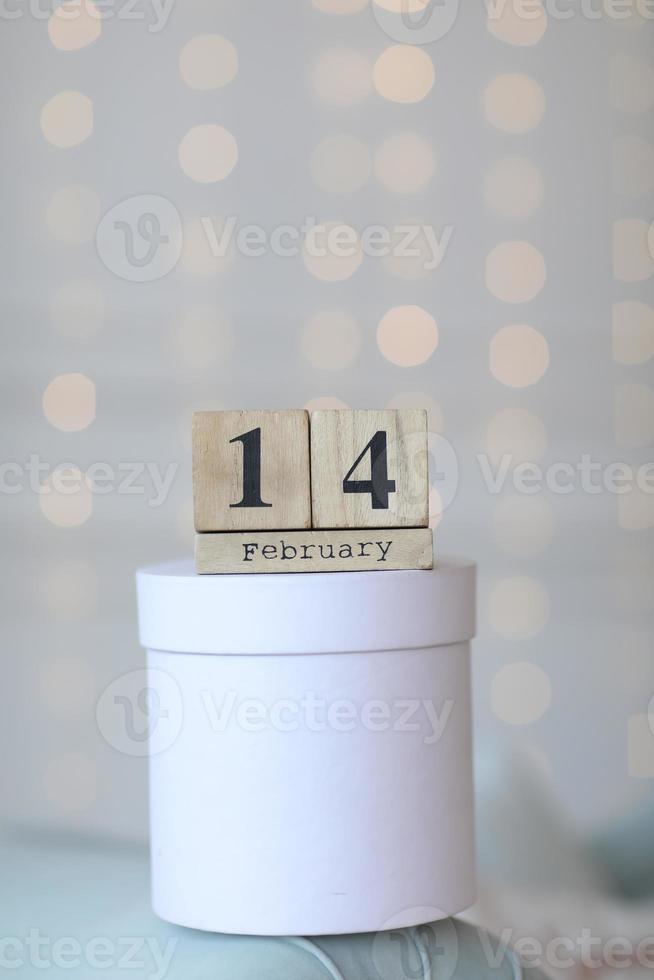 Valentine's day concept. Date 14 February on wooden cube calendar on a white gift box and white heart in hand. Bokeh golden and white background photo