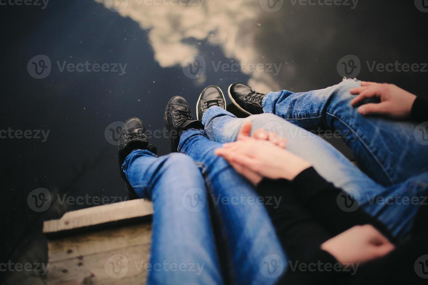 pareja amorosa sentada cerca del río en el puente tomados de la mano. foto