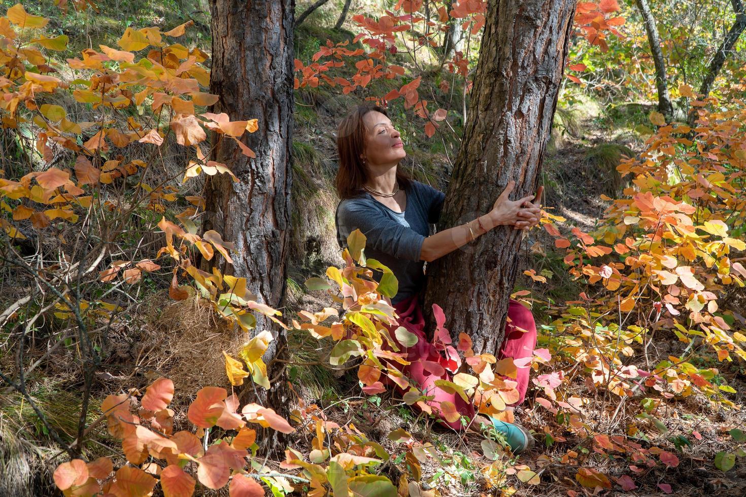 Smiling woman with red Indian pants sitting in the forest under the trees on the path with autumn foliage. Portrait of a happy woman photo