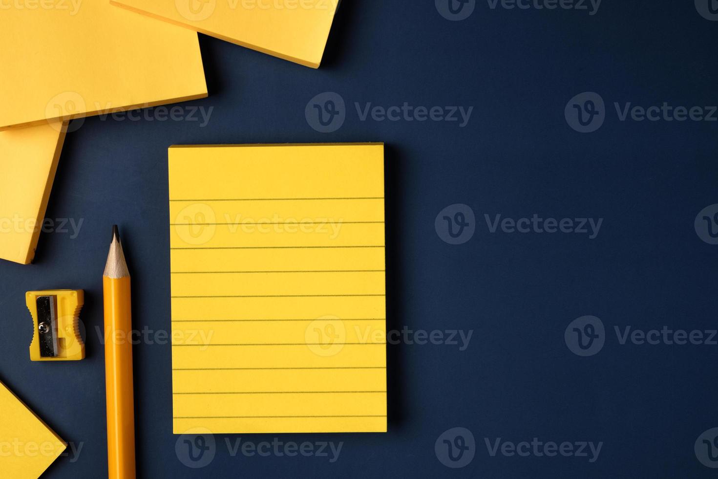 blank yellow sticky note and pencil on navy blue table background photo