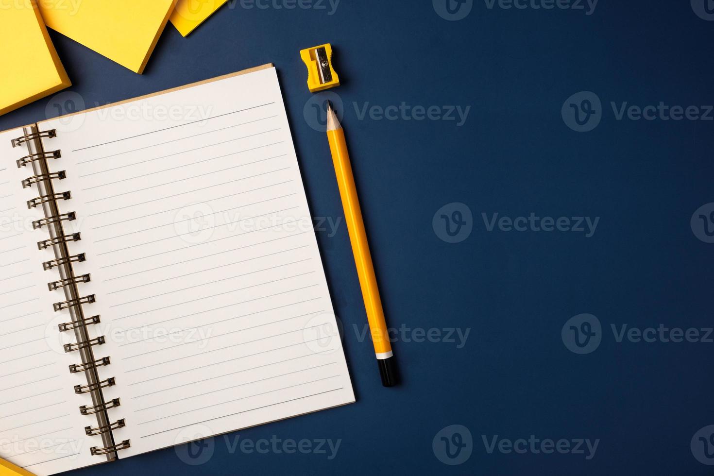 top view open notebook with yellow pencil and notepad on navy blue working table photo