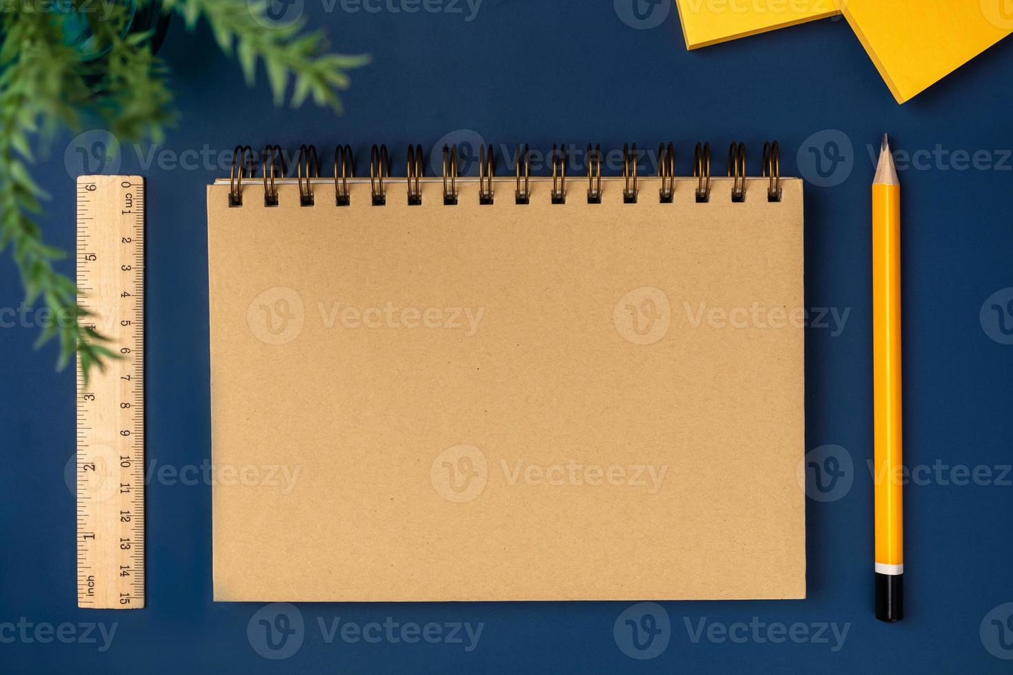 top view brown notebook with yellow pencil and notepad on navy blue working table photo