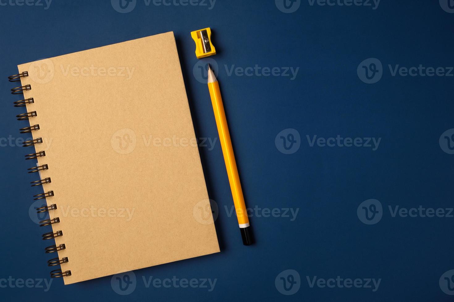 top view brown notebook with yellow pencil and notepad on navy blue working table photo