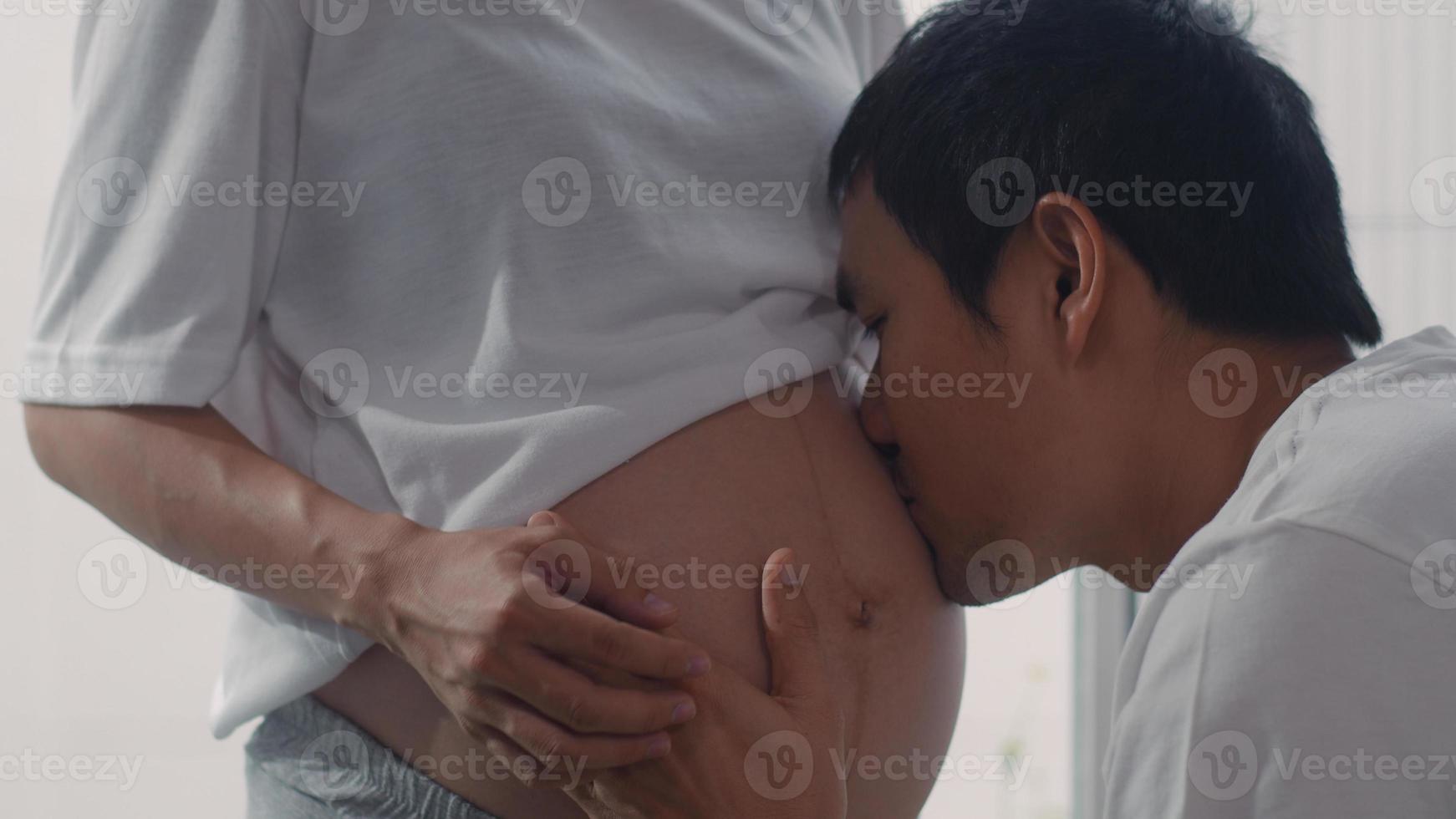 joven pareja asiática embarazada besando a su esposa en el vientre hablando con su hijo foto