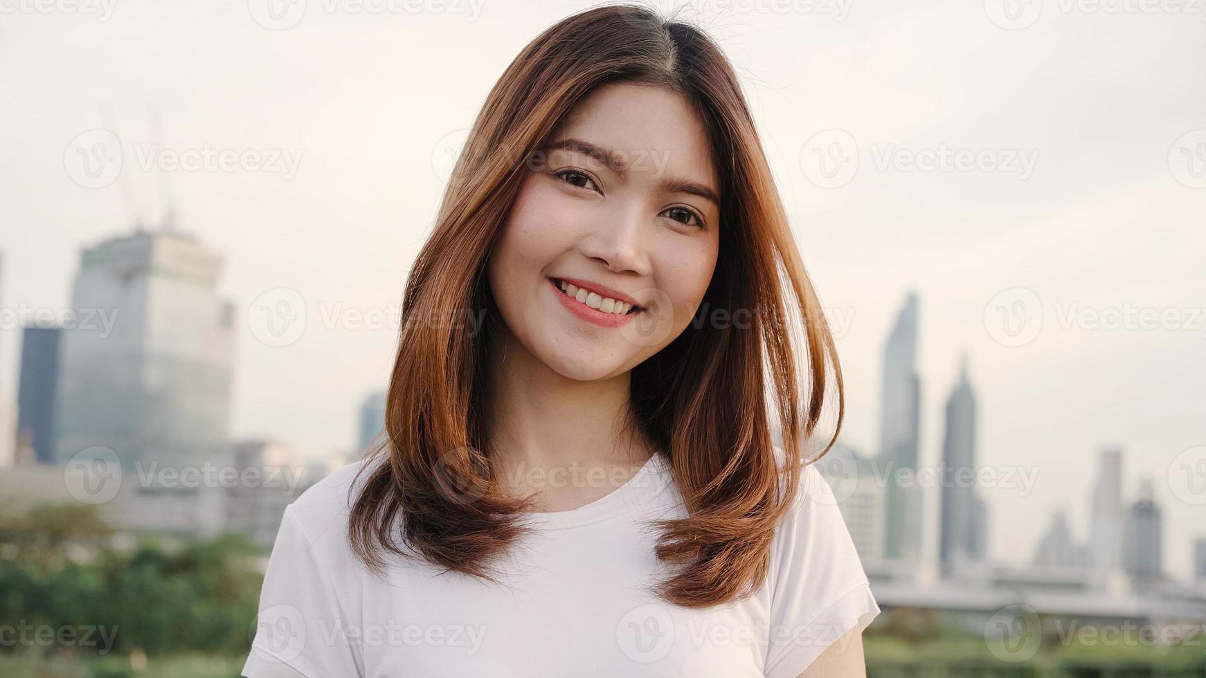 Cheerful beautiful young Asian woman feeling happy smiling to camera while traveling on the street at downtown city. Lifestyle backpack tourist travel holiday concept. Portrait looking at camera. photo