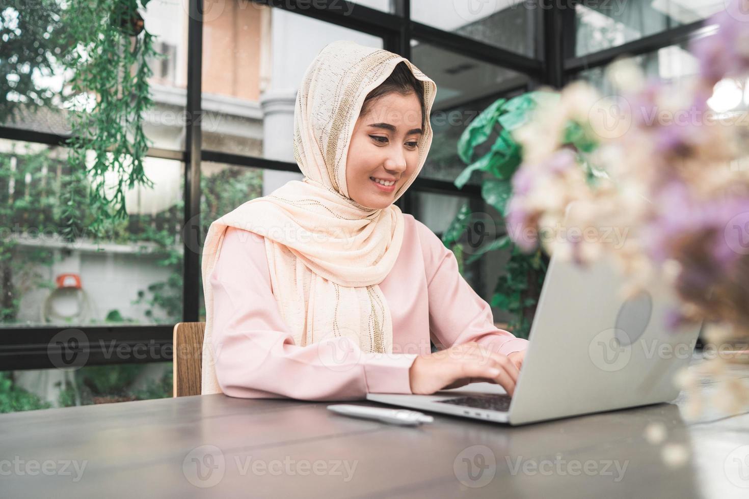 Beautiful young smiling asian muslim woman working on laptop sitting in living room at home. Asian business woman working document finance and calculator in her home office. Enjoying time at home. photo