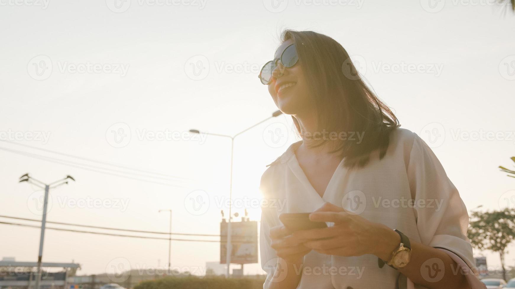 exitosa joven mujer de negocios de asia en ropa de oficina de moda saludando en la carretera tomando un taxi y sosteniendo un teléfono inteligente mientras está de pie al aire libre en una ciudad urbana moderna. concepto de negocio sobre la marcha. foto