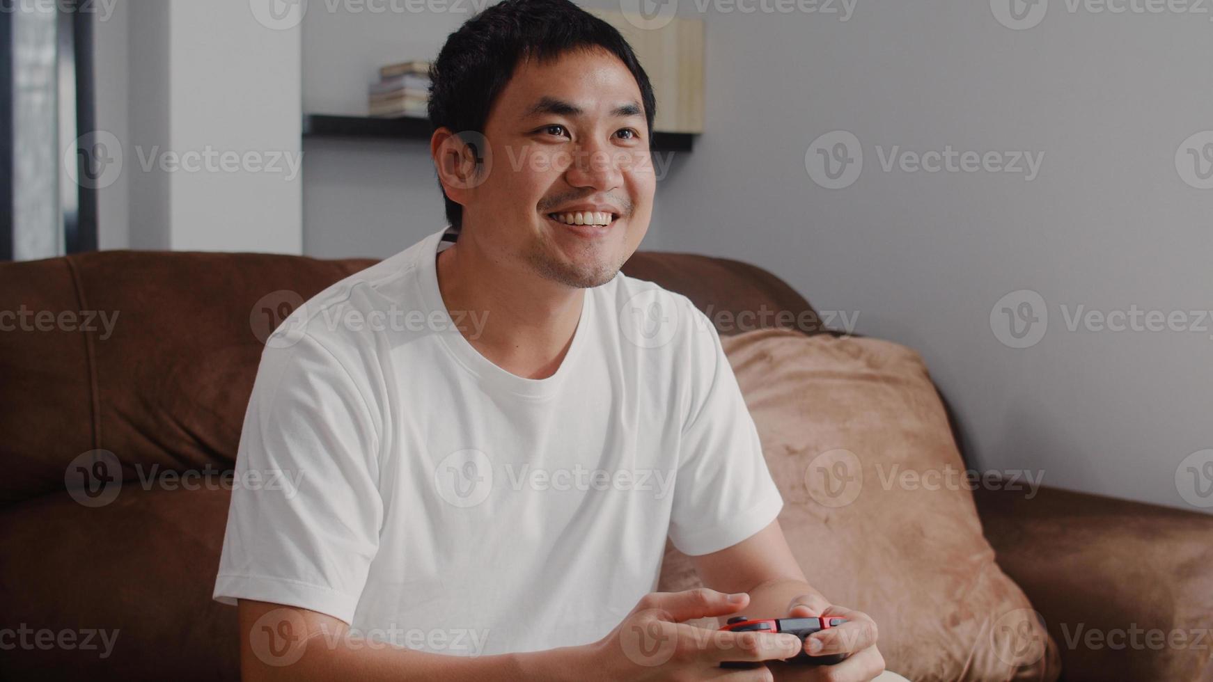 Young Asian man using joystick playing video games in television in living room, male feeling happy using relax time lying on sofa at home. Men play games relax at home concept. photo