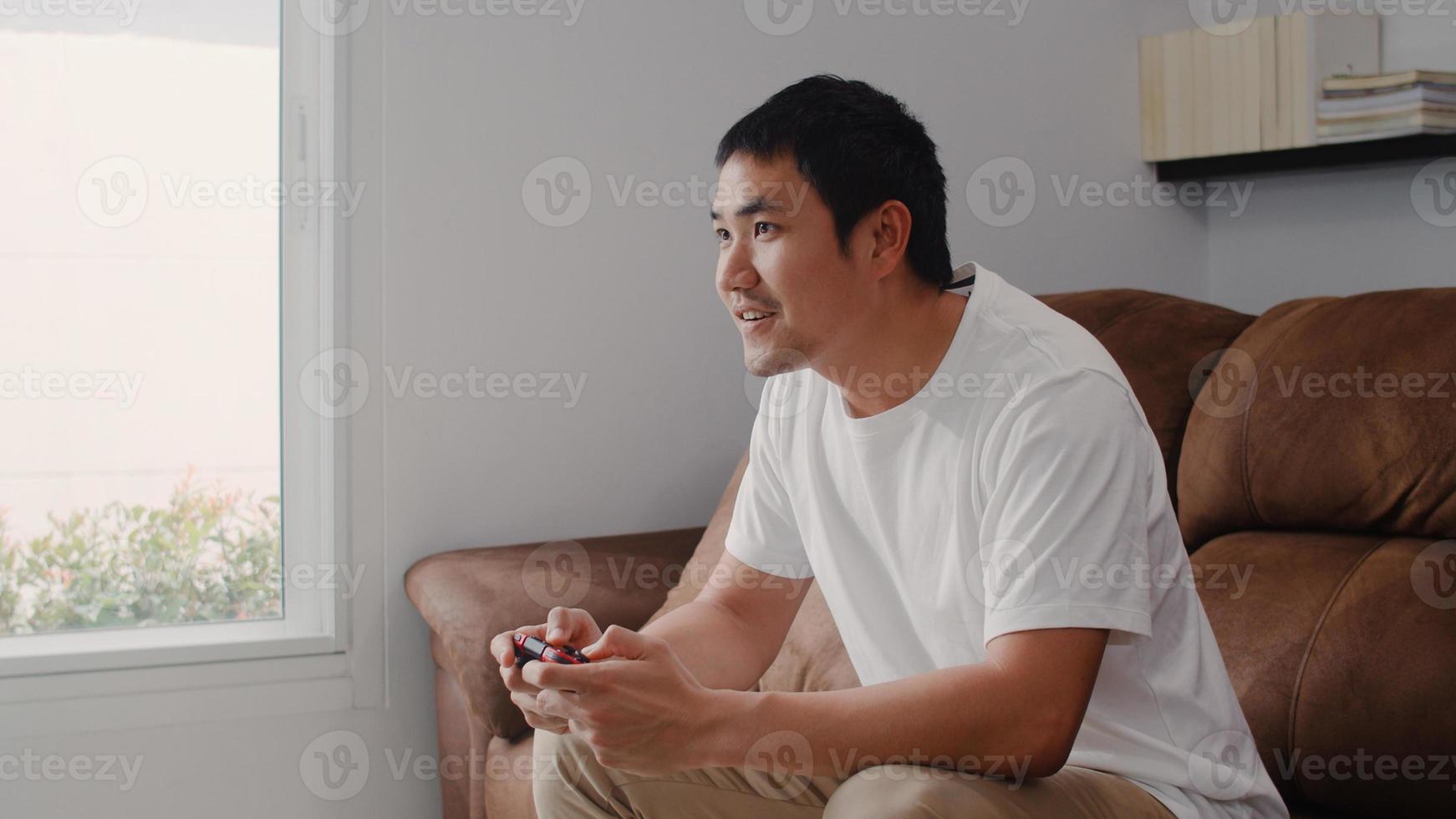 joven asiático usando joystick jugando videojuegos en la televisión en la sala de estar, el hombre se siente feliz usando el tiempo de relajación acostado en el sofá en casa. los hombres juegan y se relajan en el concepto de hogar. foto