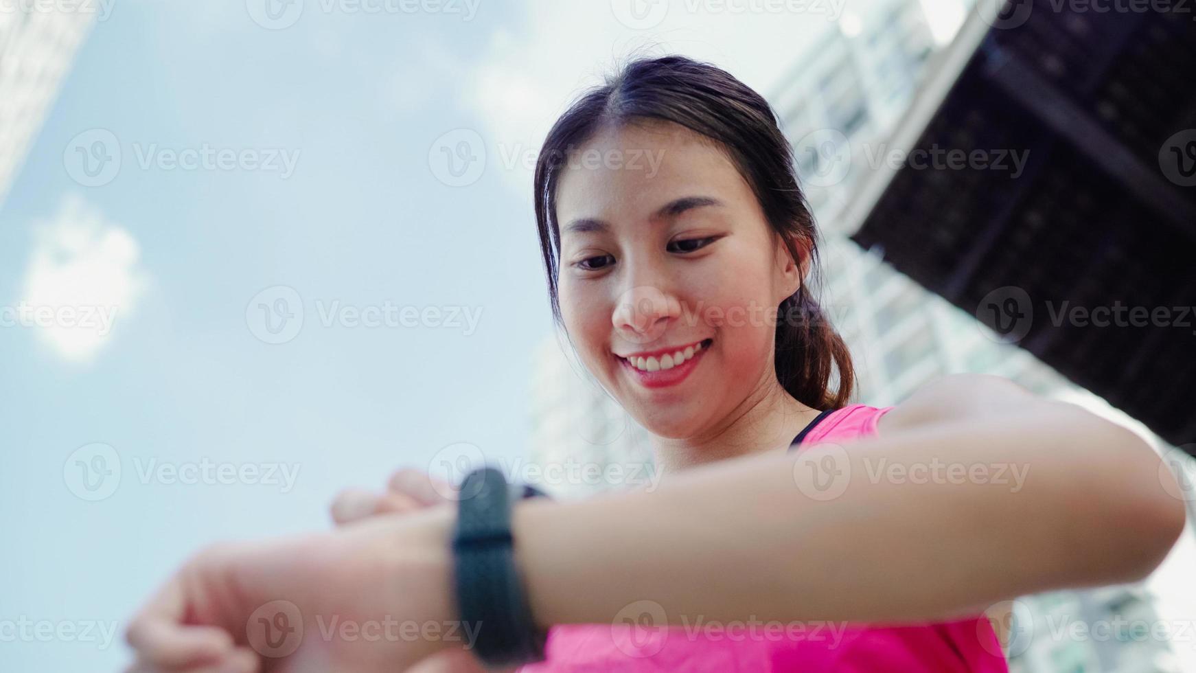 Healthy beautiful young Asian Athlete woman setting and checking progress looking heart rate monitor on smart watch while running in urban city. Lifestyle women exercise in the city concept. photo