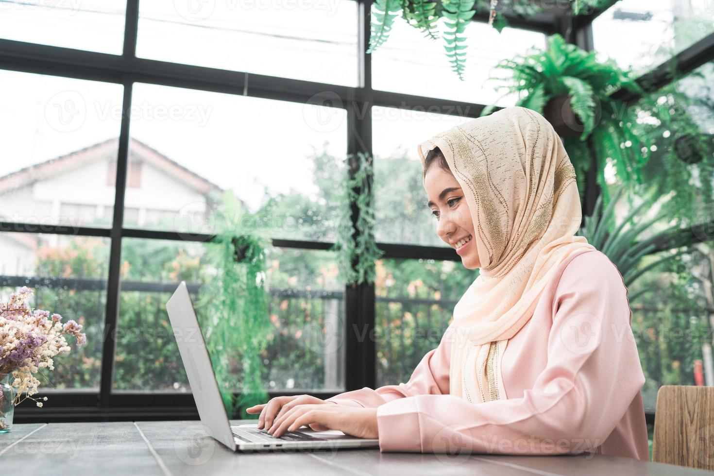 Beautiful young smiling asian muslim woman working on laptop sitting in living room at home. Asian business woman working document finance and calculator in her home office. Enjoying time at home. photo
